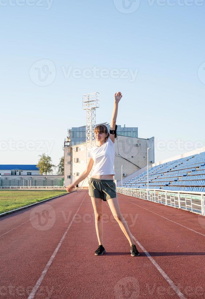 joven deportista de pie en la pista levantando los brazos foto