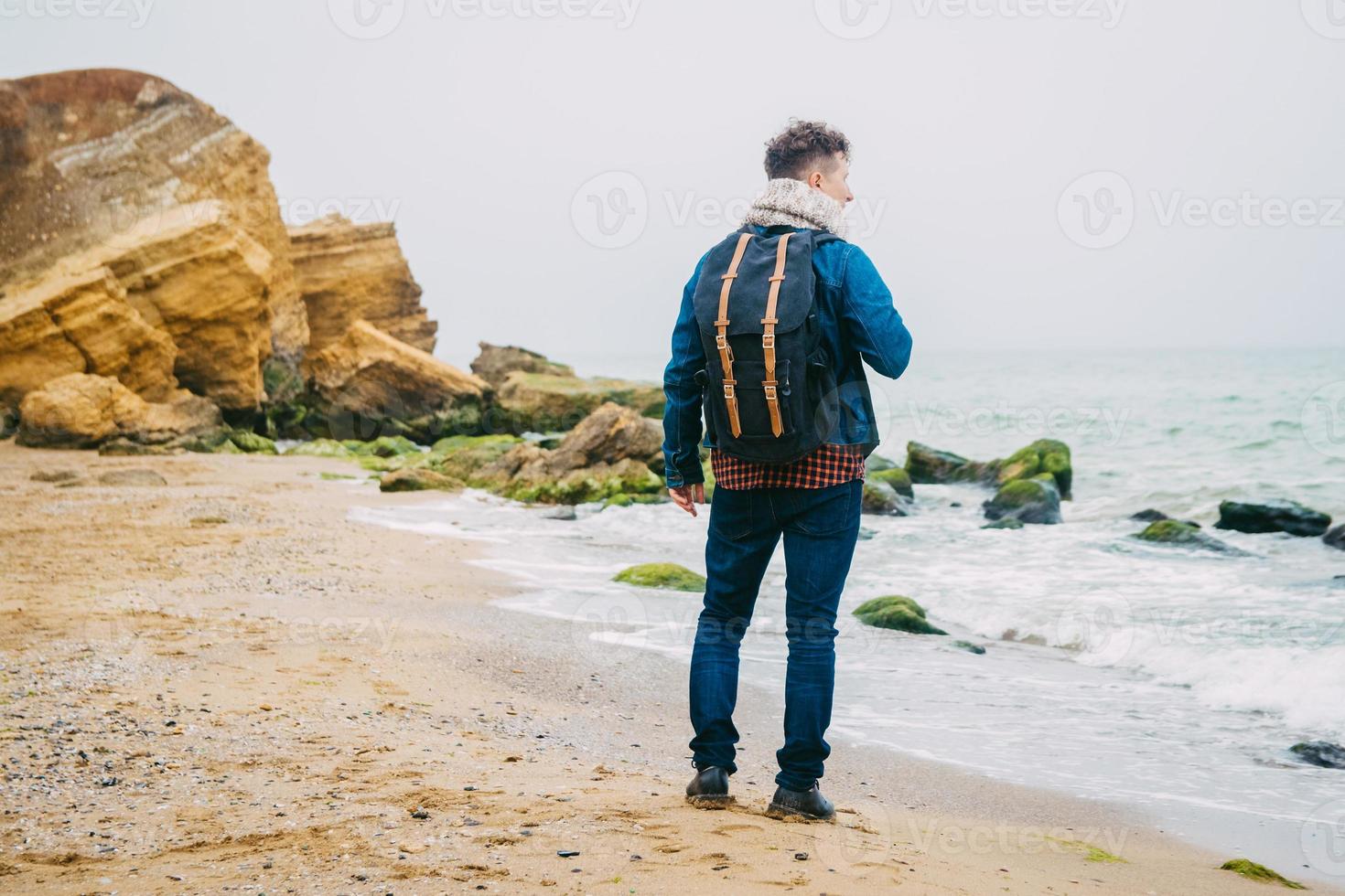 Hombre con una mochila de pie sobre una roca frente a un hermoso mar foto