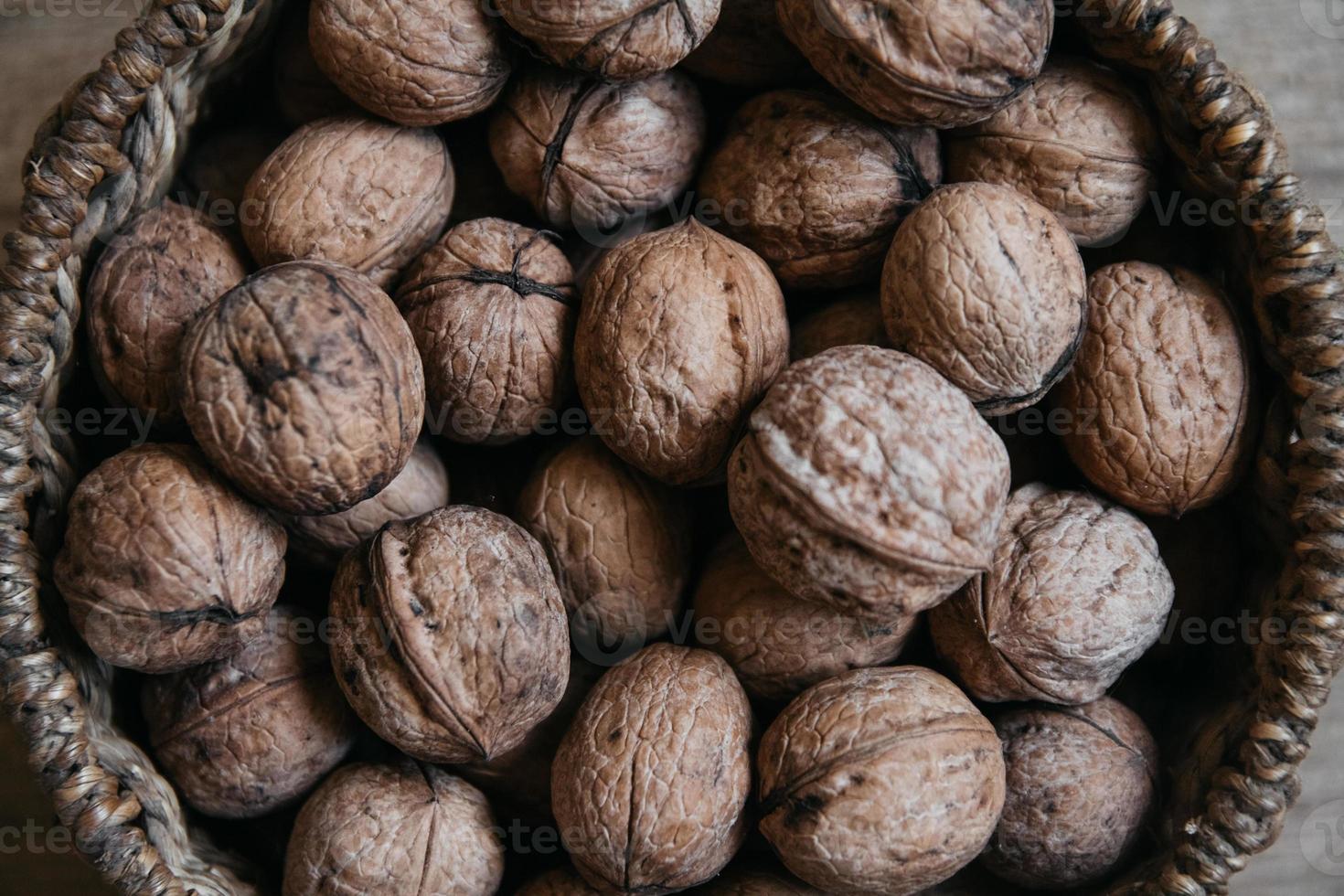 Walnuts in a round wicker basket on a wooden background. Close up. photo