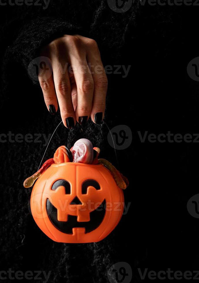 mano de halloween de mujer con uñas negras sosteniendo dulces de calabaza en la oscuridad foto