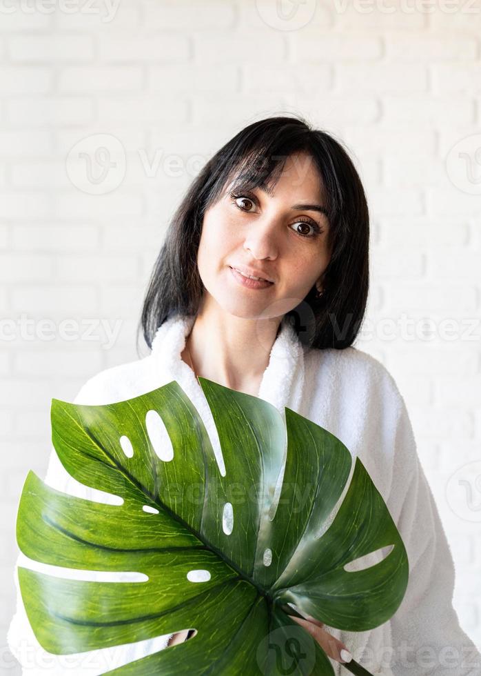 Mujer de Oriente Medio vistiendo toallas de baño sosteniendo una hoja de monstera verde foto