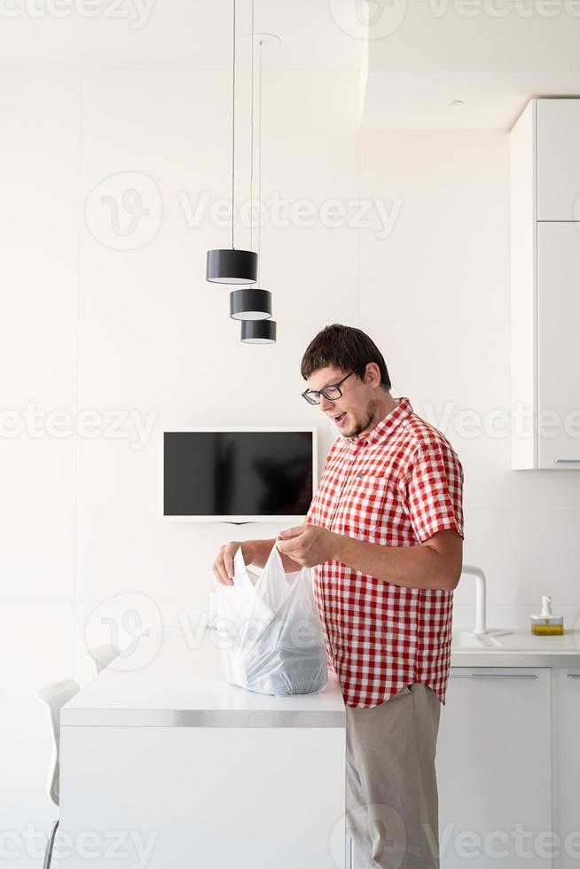 Hombre sujetando una bolsa desechable con entrega de comida en una cocina moderna foto