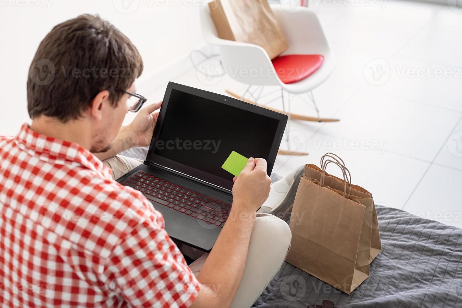 Back view of man shopping on internet with laptop looking photo