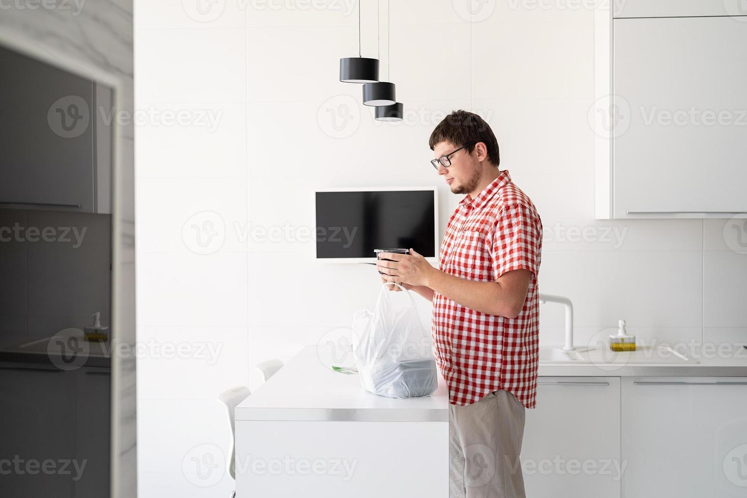 Hombre sujetando una bolsa de plástico desechable con entrega de comida en la cocina foto