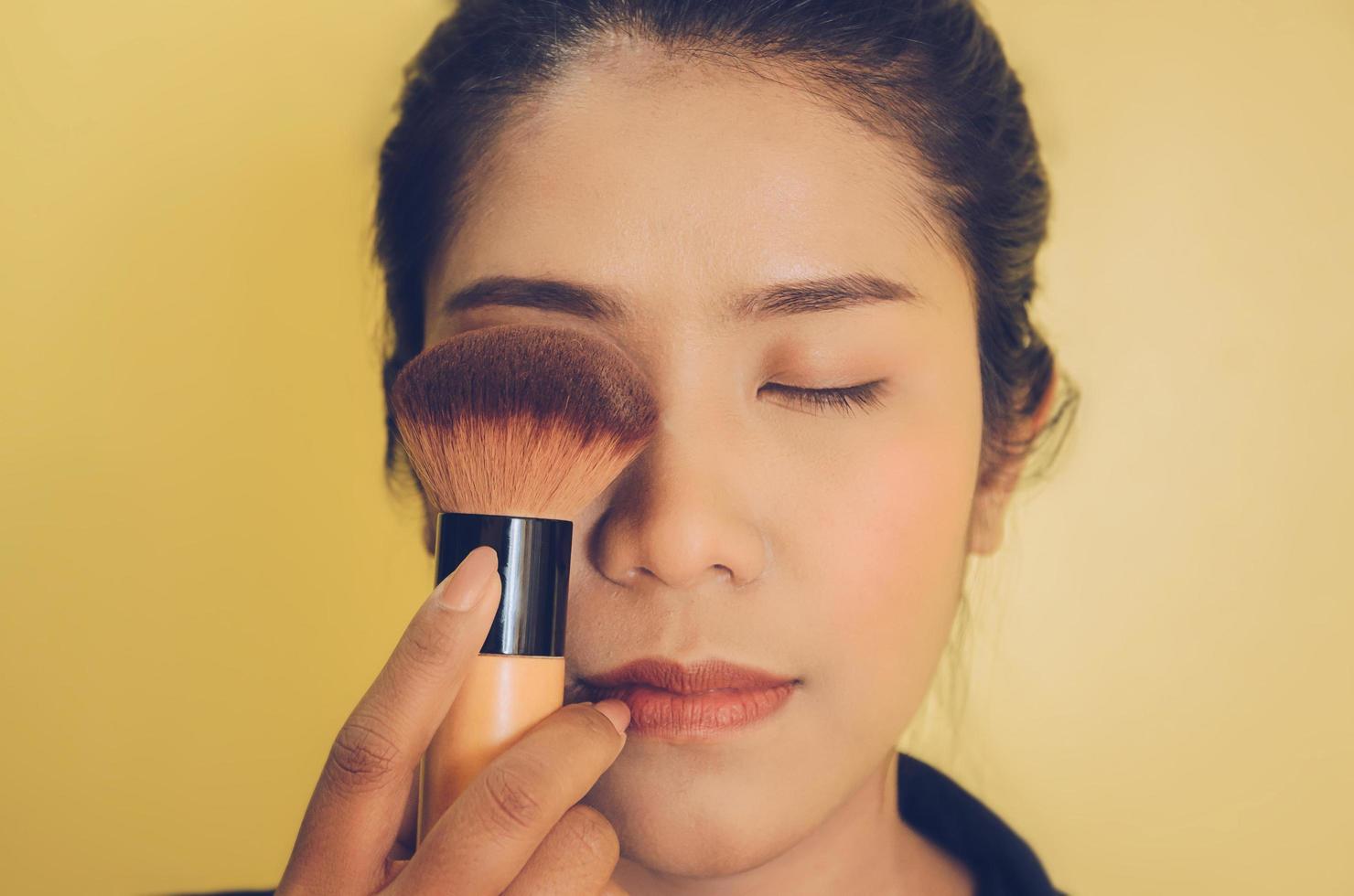 rostro de belleza de mujer asiática mediante la aplicación de pinceles en la piel con cosméticos. foto