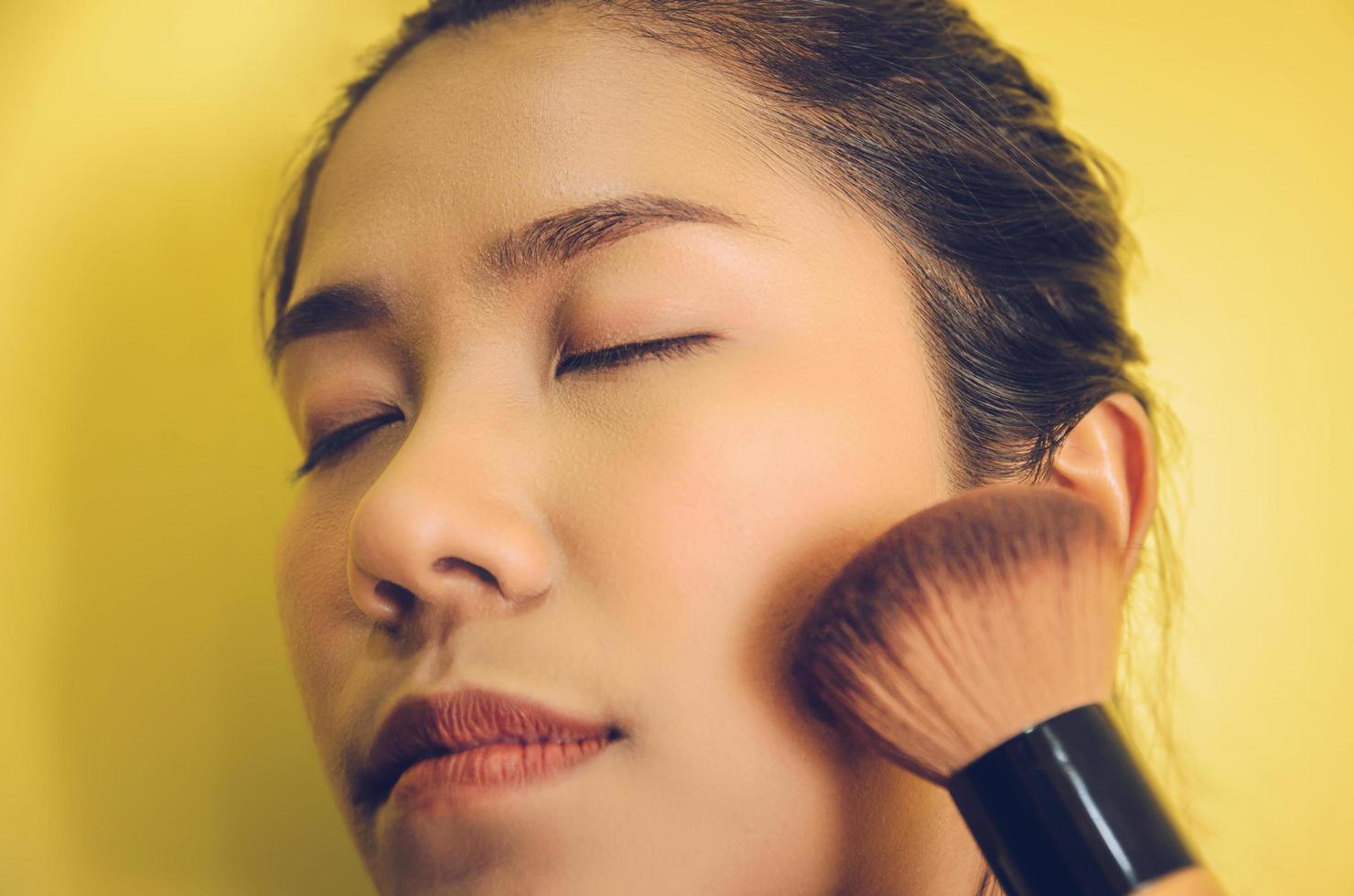 rostro de belleza de mujer asiática mediante la aplicación de pinceles en la piel con cosméticos. foto