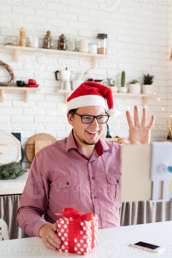 Hombre con gorro de Papá Noel saludando a sus amigos en video chat o llamada en tableta foto