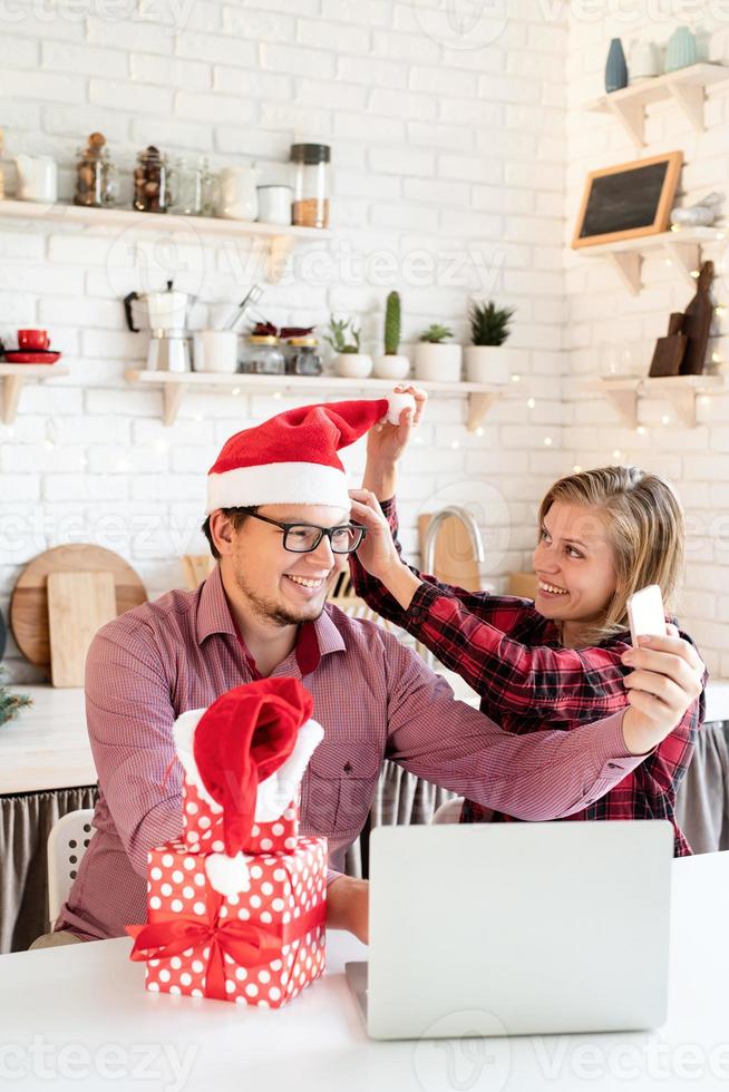 Pareja con gorro de Papá Noel saludando a sus amigos en una videollamada en tableta foto