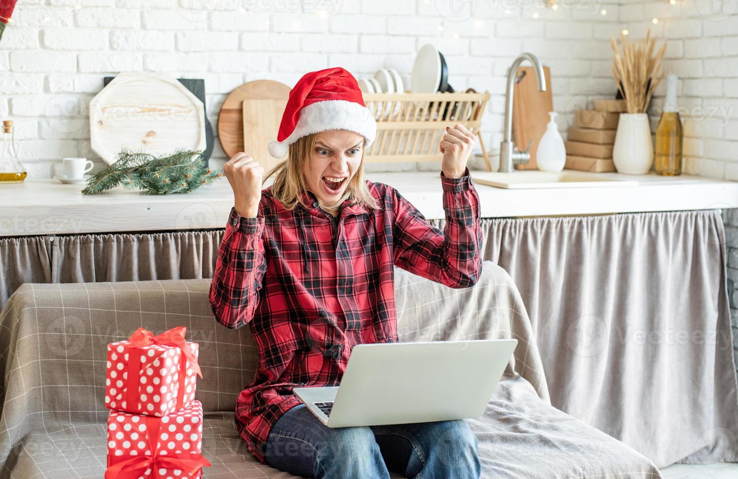 Woman in santa hat screaming raising her hands working at the laptop photo