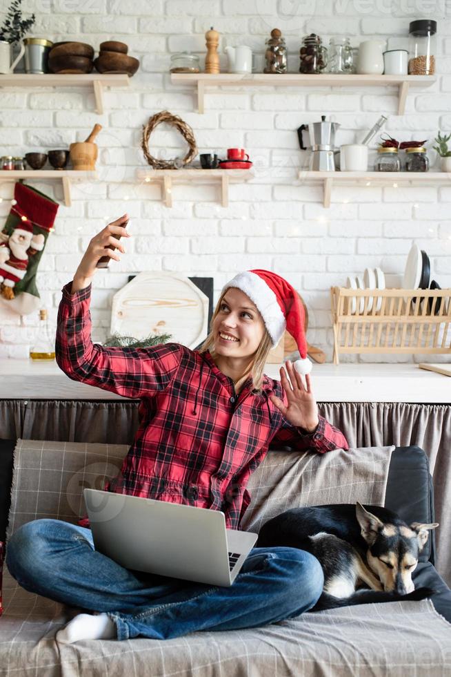 Young woman in santa hat greeting her friends in video chat on laptop photo