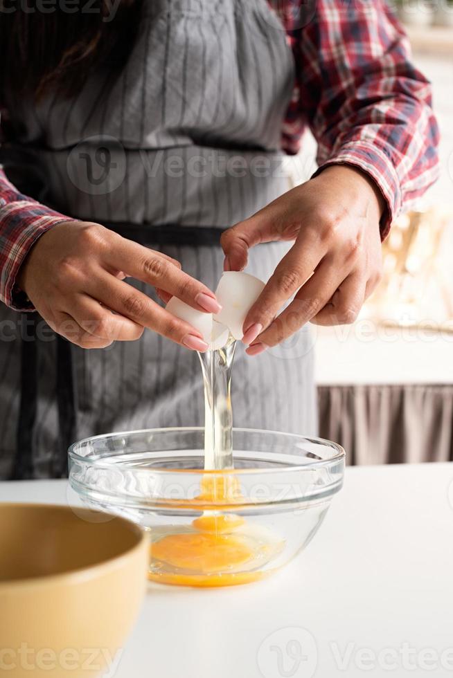 Manos de mujer rompiendo el huevo en la cocina. foto