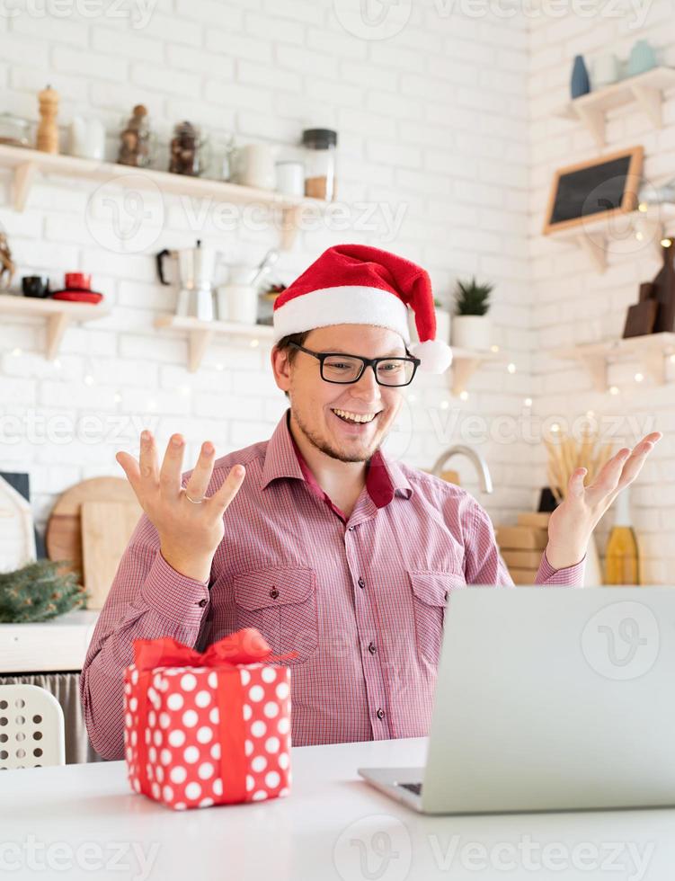 Man in santa hat greeting his friends in video chat or call on laptop photo