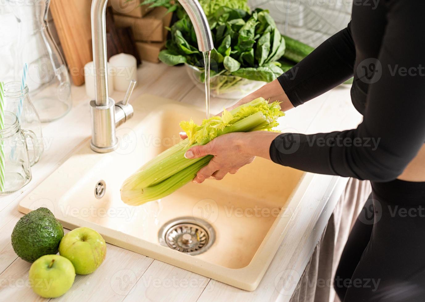 Mujer lavando apio en el fregadero de la cocina foto