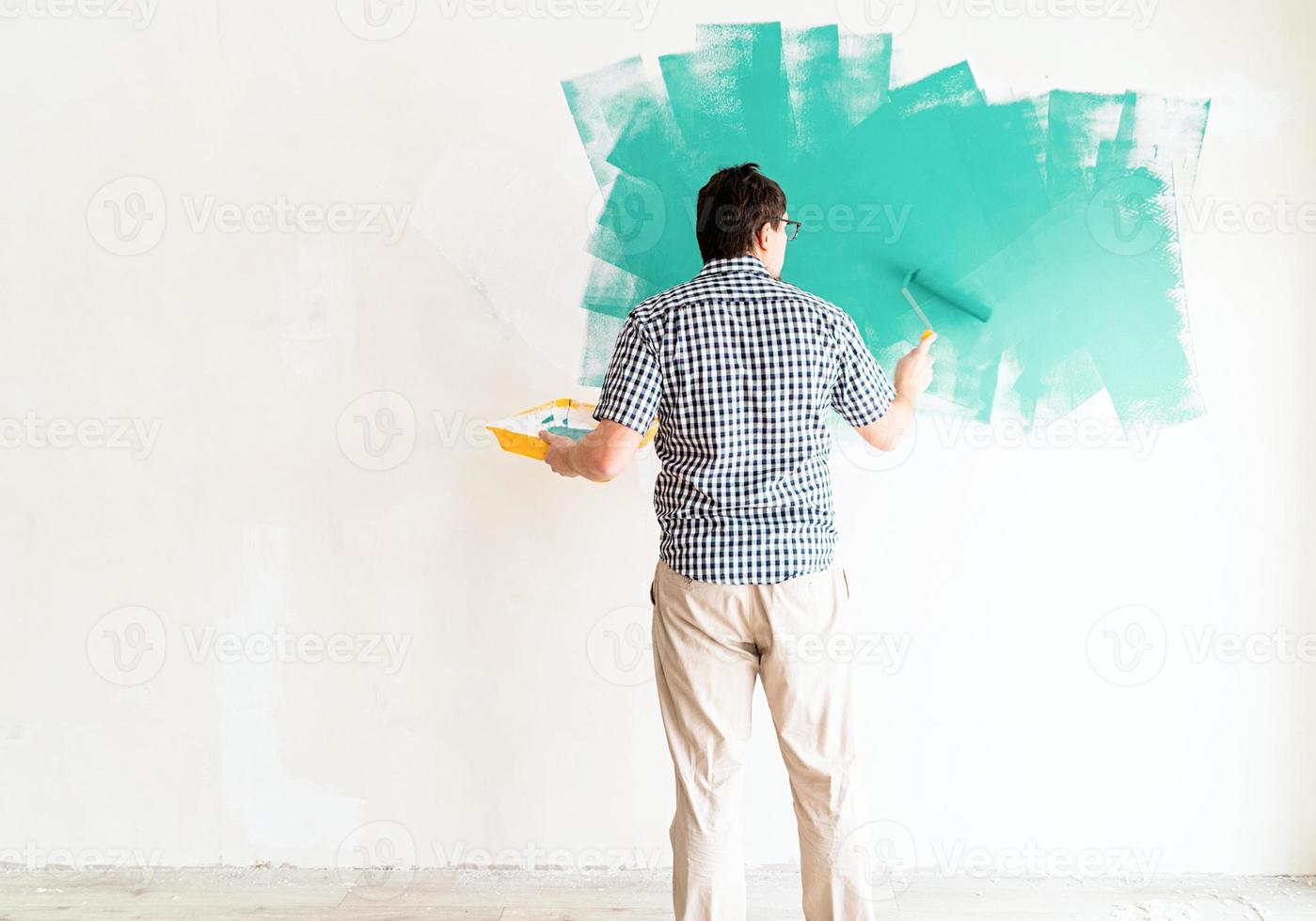 Hombre coloreando la pared verde con un rodillo foto