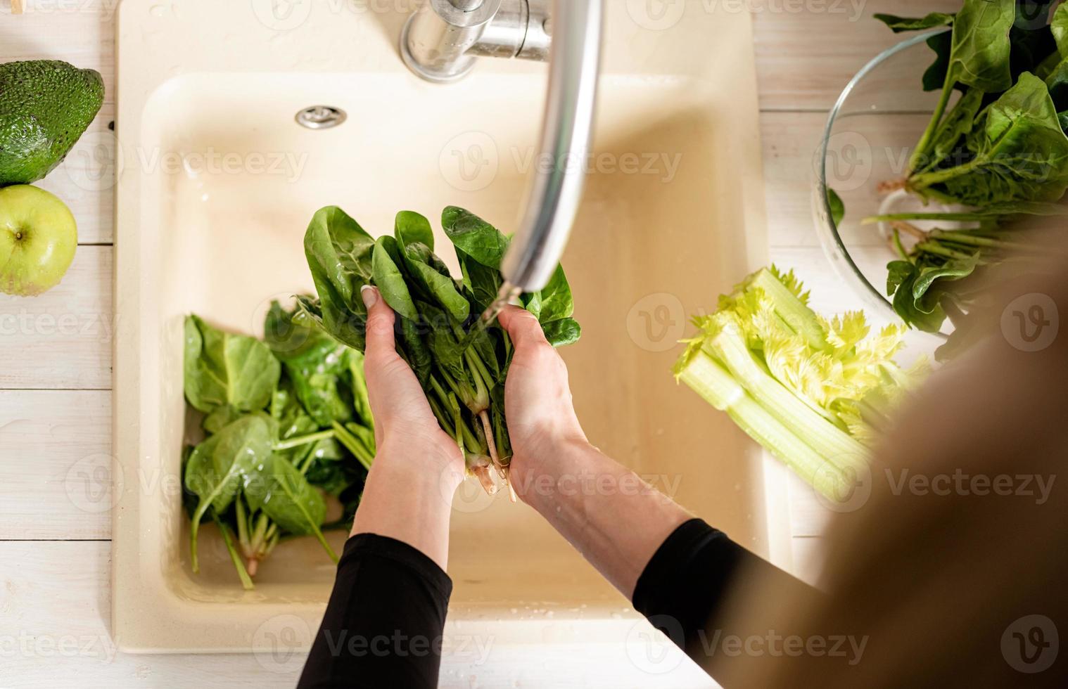 Vista superior de la mujer lavando las manos espinacas en el fregadero de la cocina foto