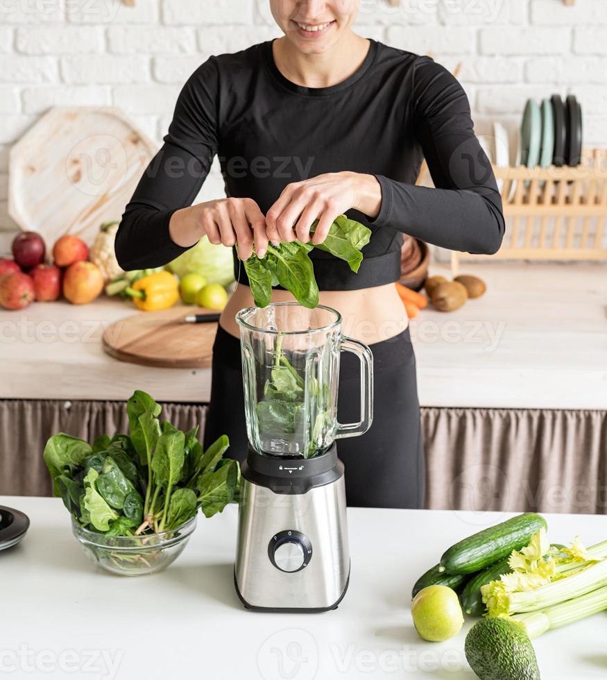 Young blond smiling woman making spinach smoothie at home kitchen photo