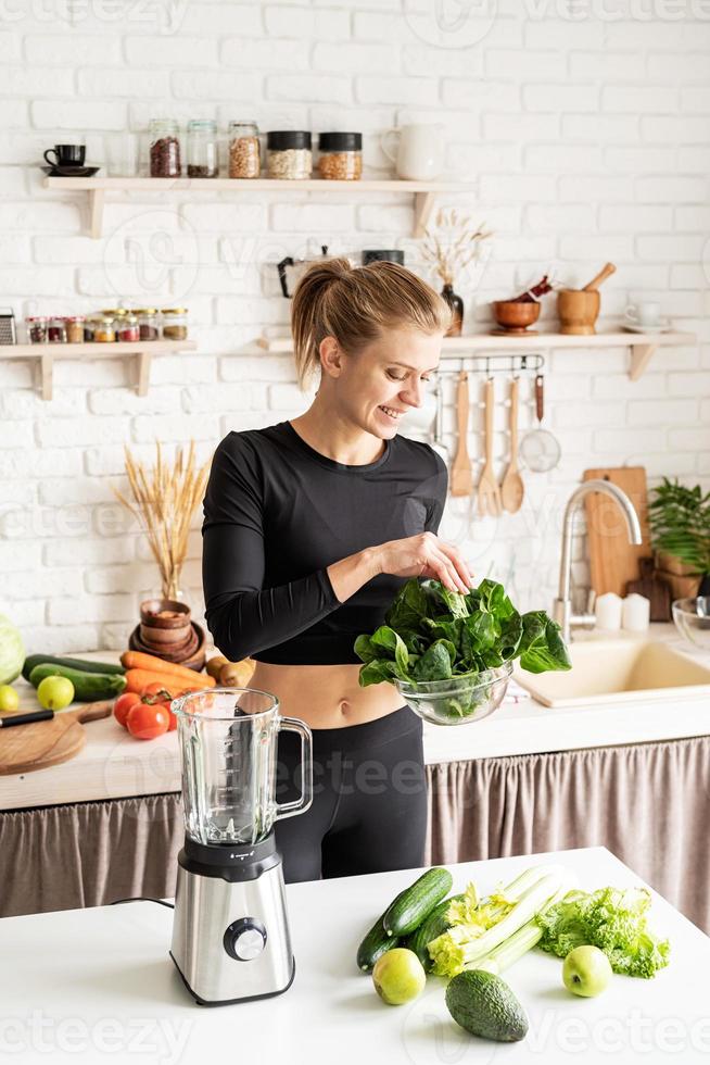 Young blond smiling woman making spinach smoothie at home kitchen photo