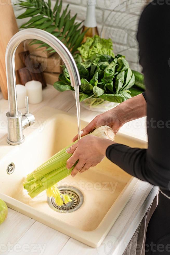 oung smiling woman in sport clothes washing celery in the kitchen photo