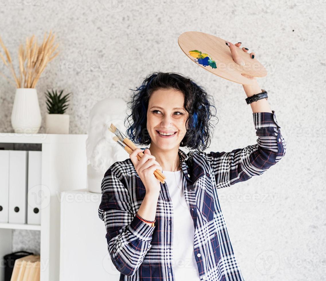 Woman artist in her studio holding art palette and paintbrushes photo