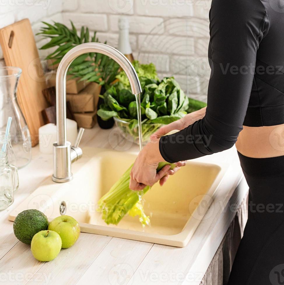 Mujer lavando apio en el fregadero de la cocina foto