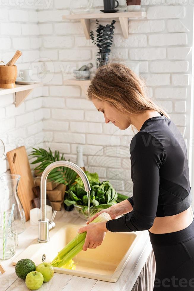 Mujer lavando apio en el fregadero de la cocina foto