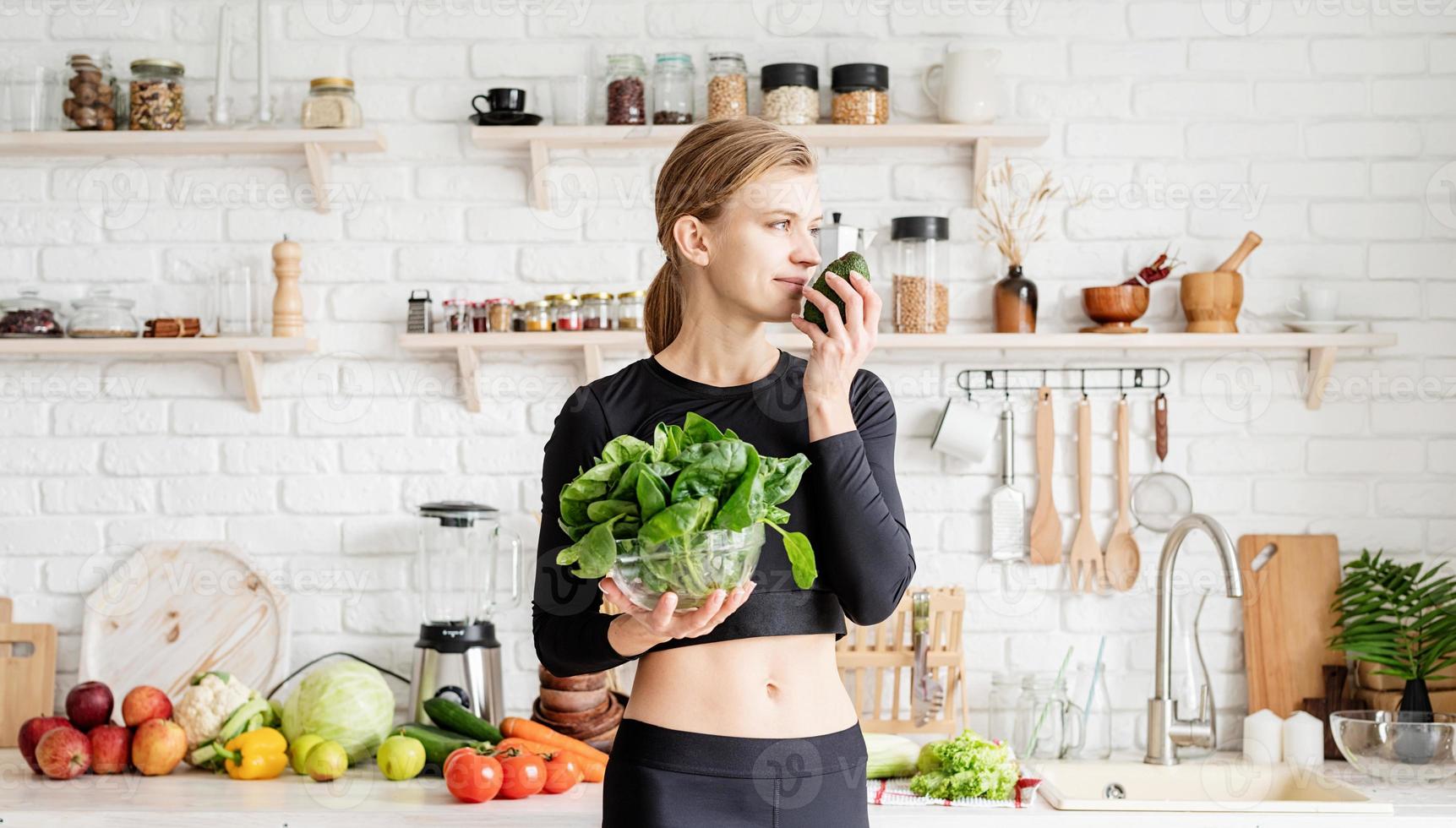 Mujer en ropa deportiva sosteniendo un plato de espinacas frescas en la cocina foto