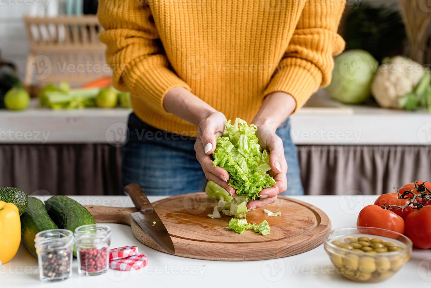 Mujer preparando ensalada griega en la cocina cortando lechuga foto