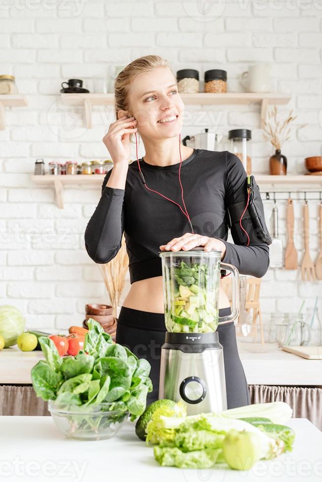 Mujer haciendo batido verde en la cocina de casa foto