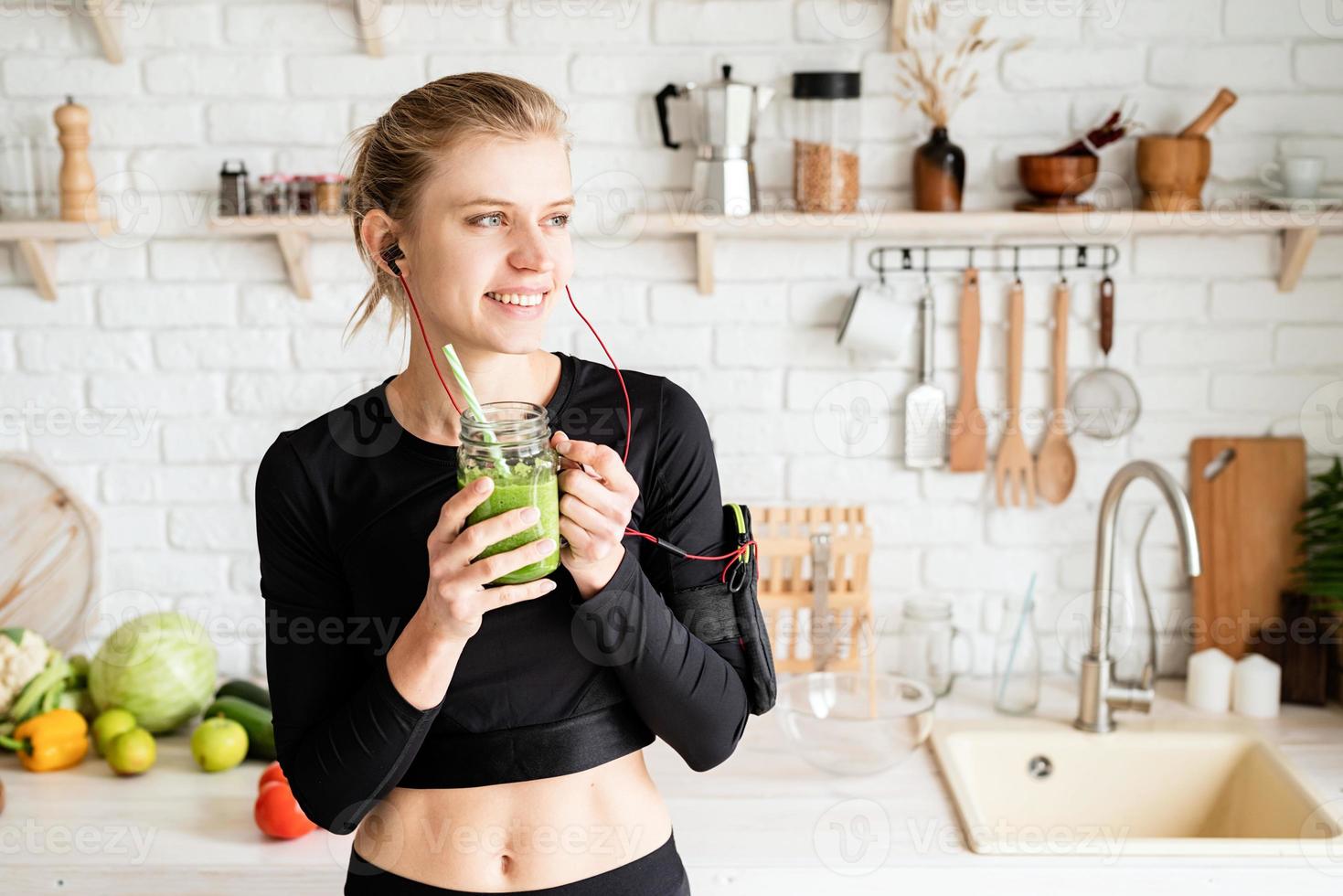 Woman drinking green smoothie from mason jar at home kitchen photo