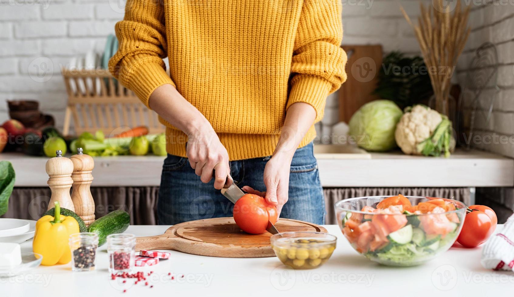 Manos femeninas haciendo ensalada cortando tomates en la cocina foto