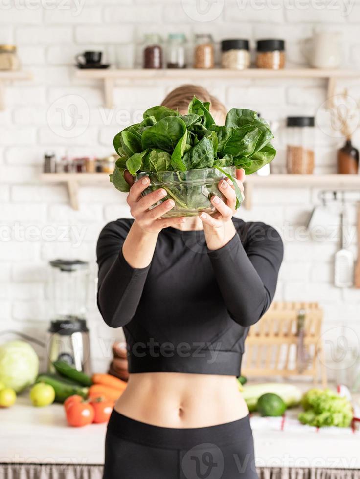 Mujer sonriente sosteniendo un plato de espinacas frescas en la cocina foto