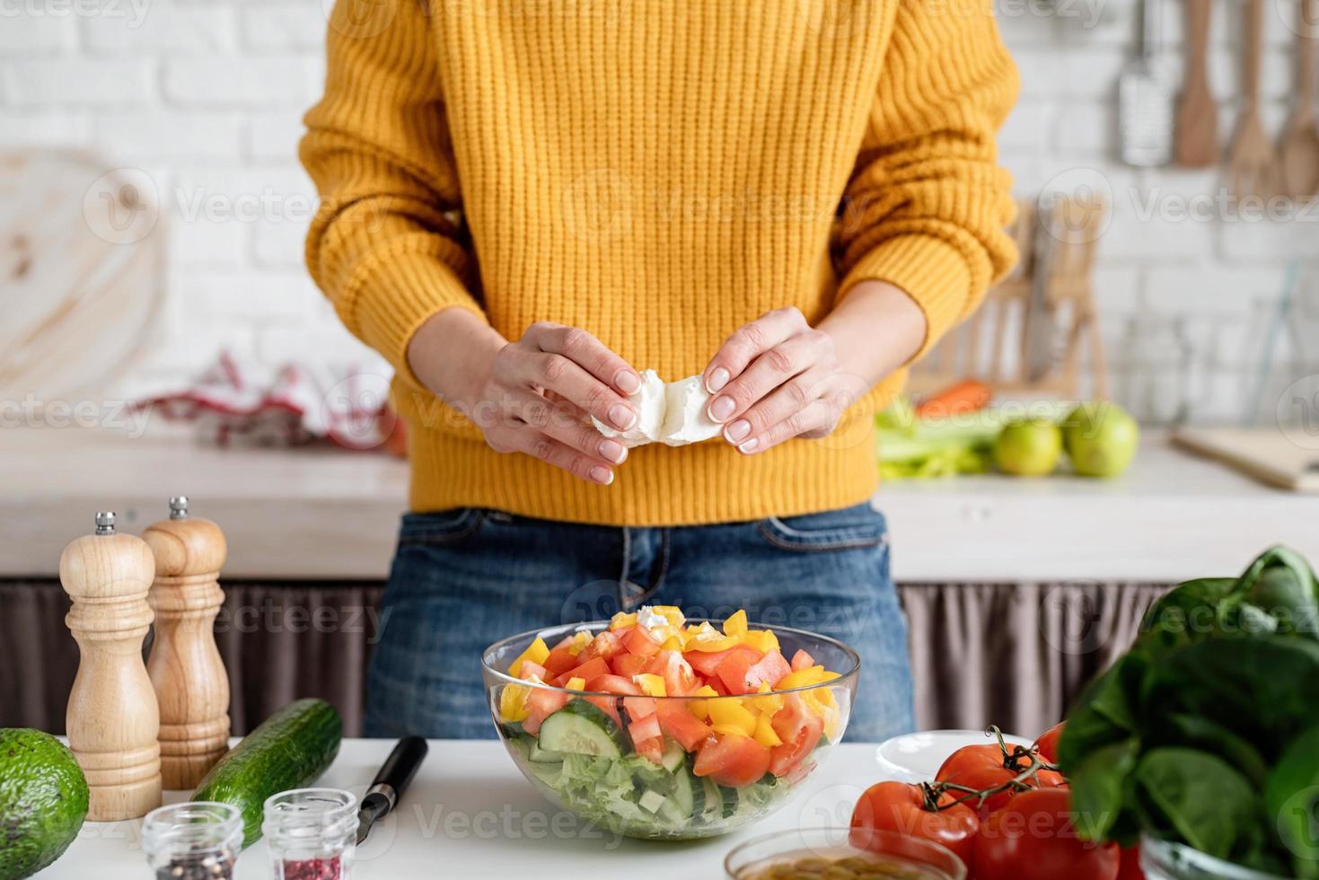 Manos femeninas haciendo ensalada cortando queso feta en la cocina foto