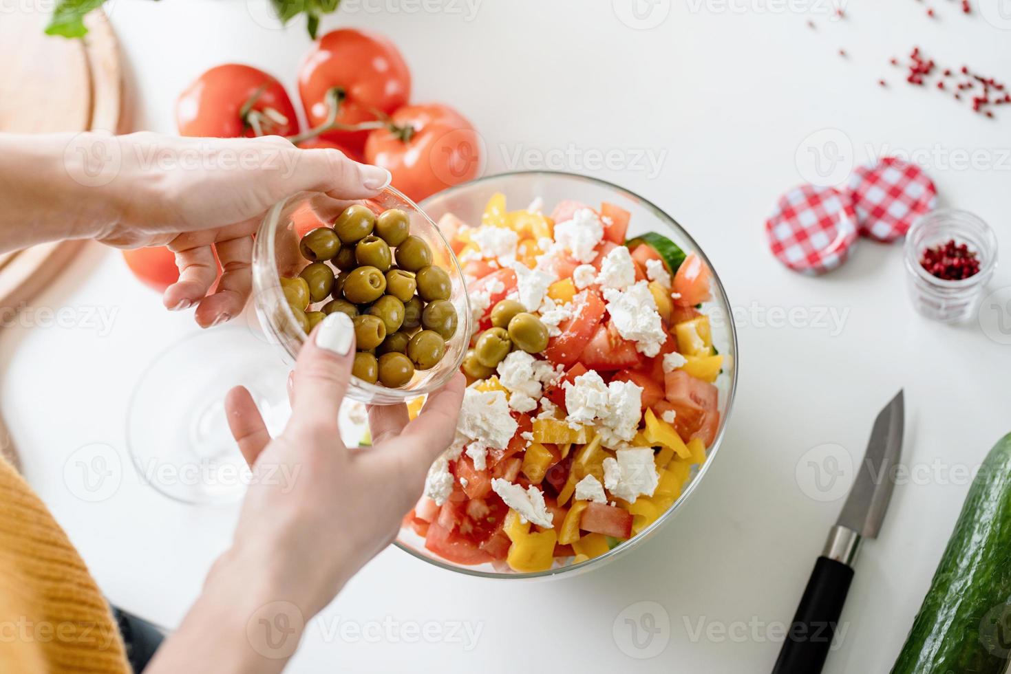 Manos femeninas haciendo ensalada griega agregando aceitunas al cuenco foto