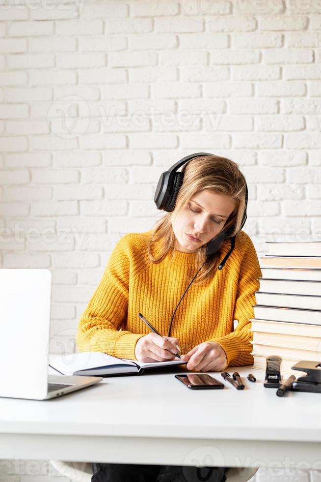 Woman studying online using laptop writing in notebook photo