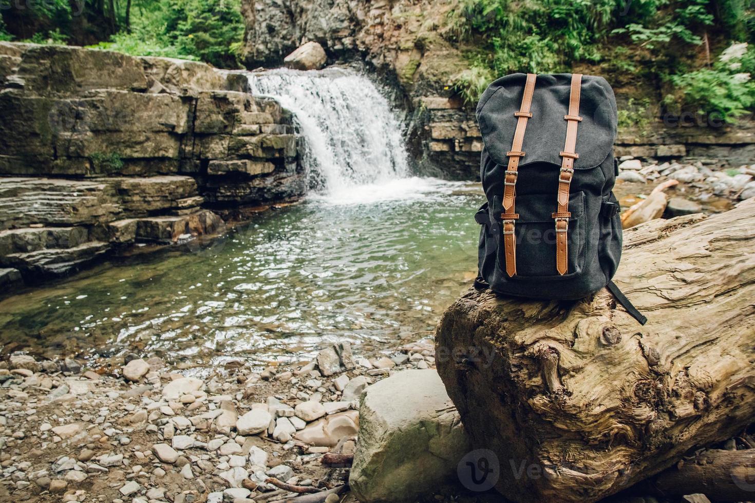 Hipster hiker tourist backpack on background of river and waterfall photo