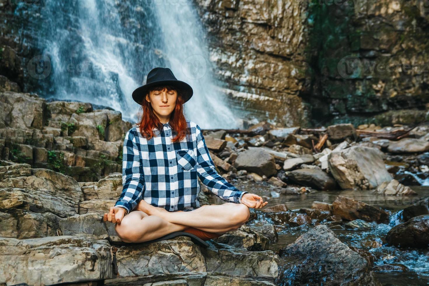 Woman in a hat and shirt meditating on rocks in a lotus position photo