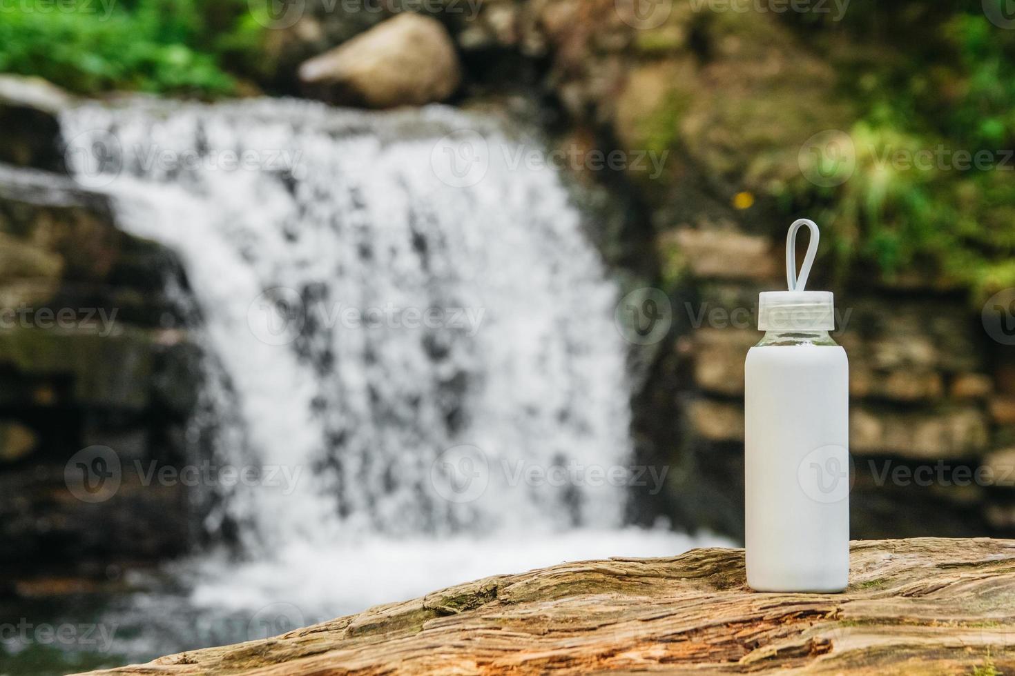 Botella blanca sobre un tronco de madera contra el fondo de la cascada foto