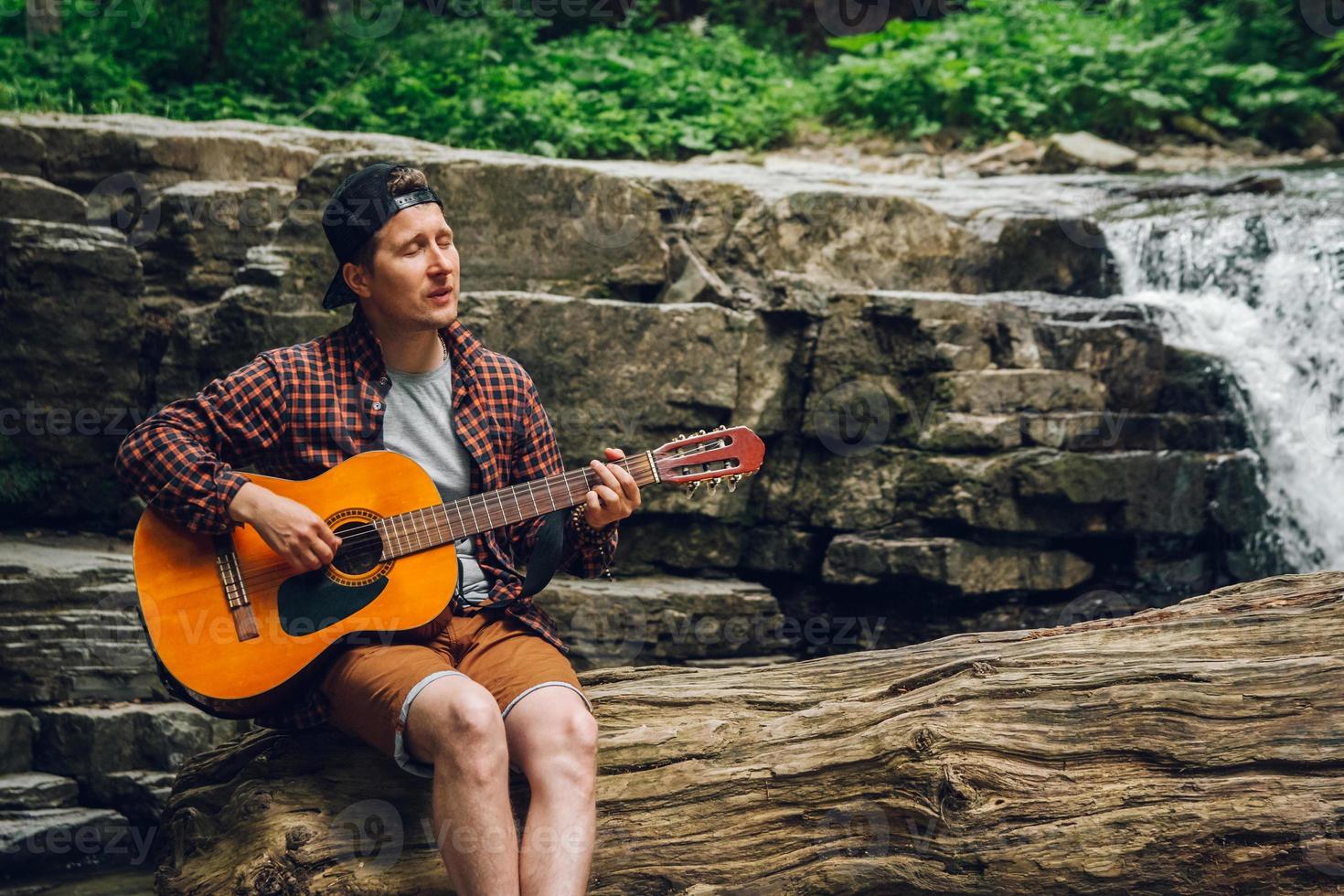 hombre tocando la guitarra sentado junto a una cascada foto