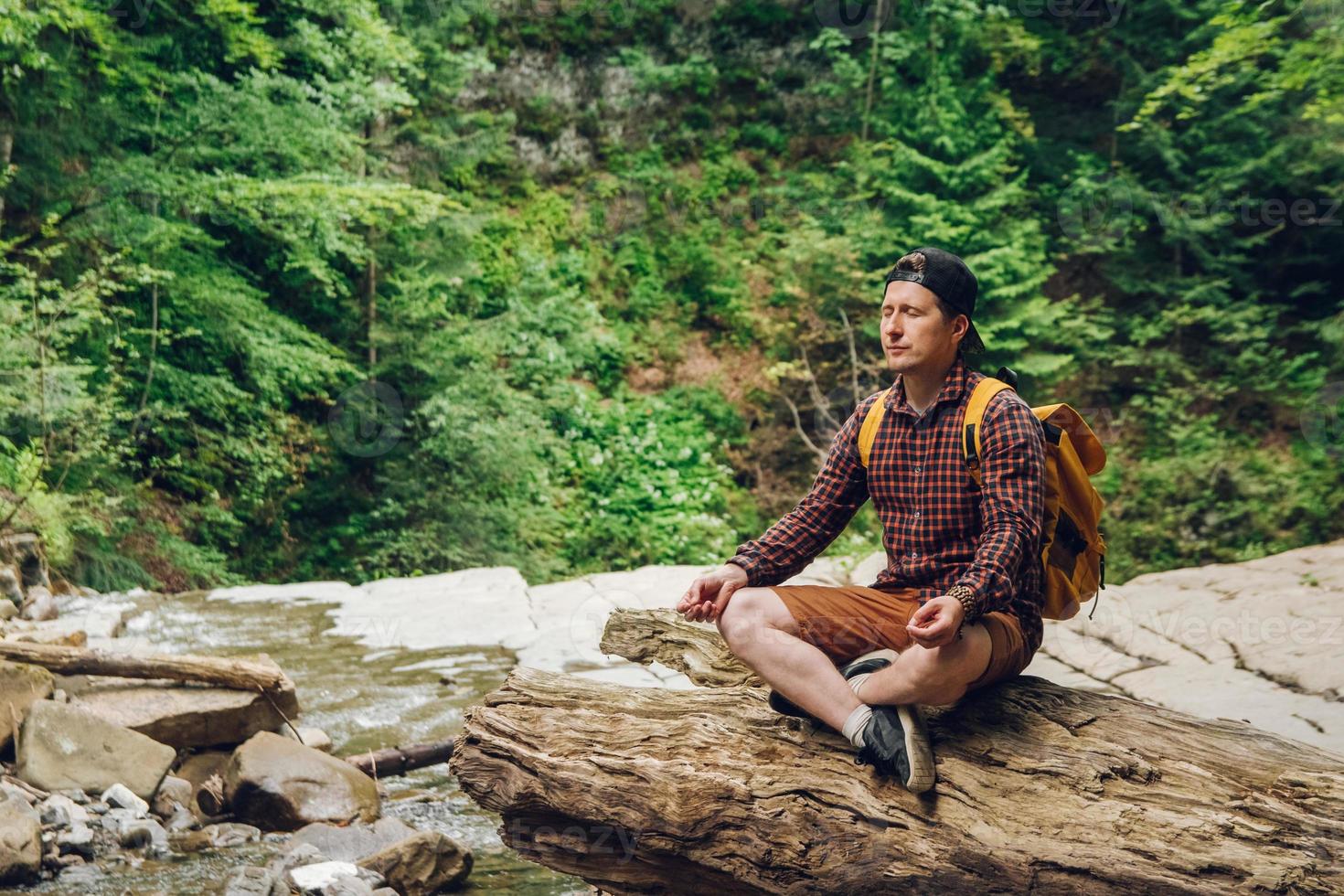 Man meditating in forest with a river photo