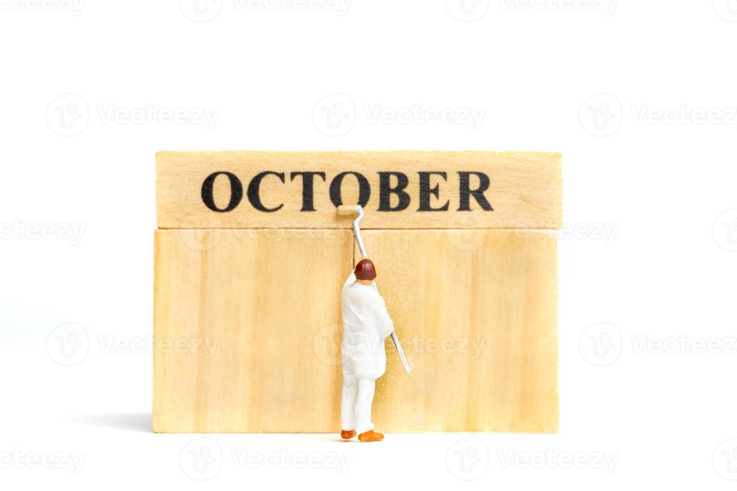 Gente en miniatura, trabajador pintando octubre en bloque de madera sobre fondo blanco. foto