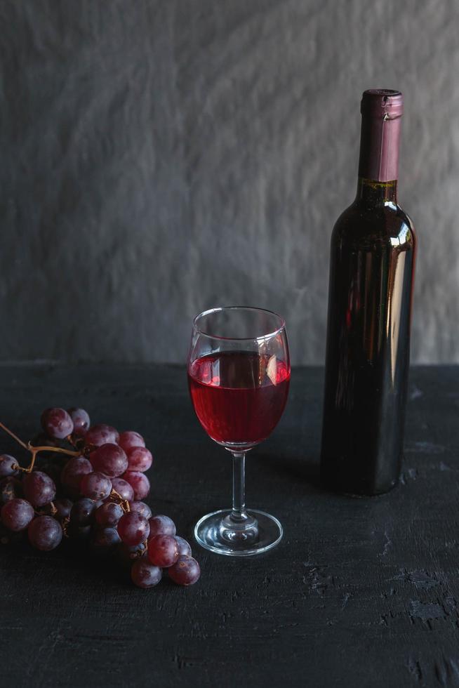 Botella de vino tinto y vino con uvas sobre fondo negro foto