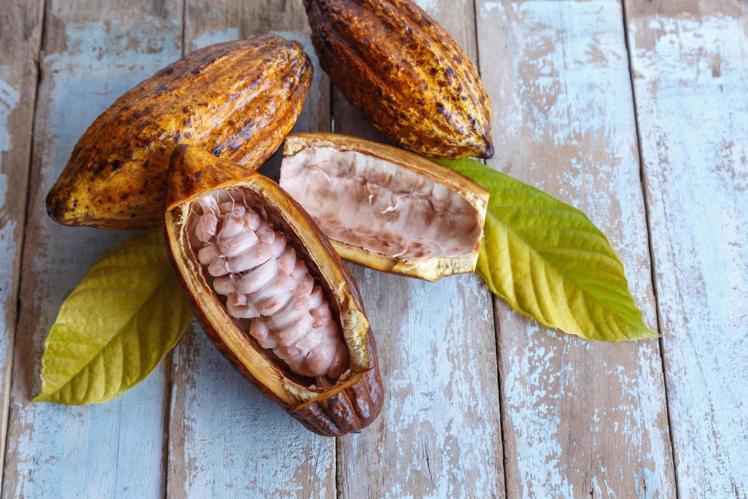 Las mazorcas de cacao frescas y hojas de cacao sobre fondo de madera foto