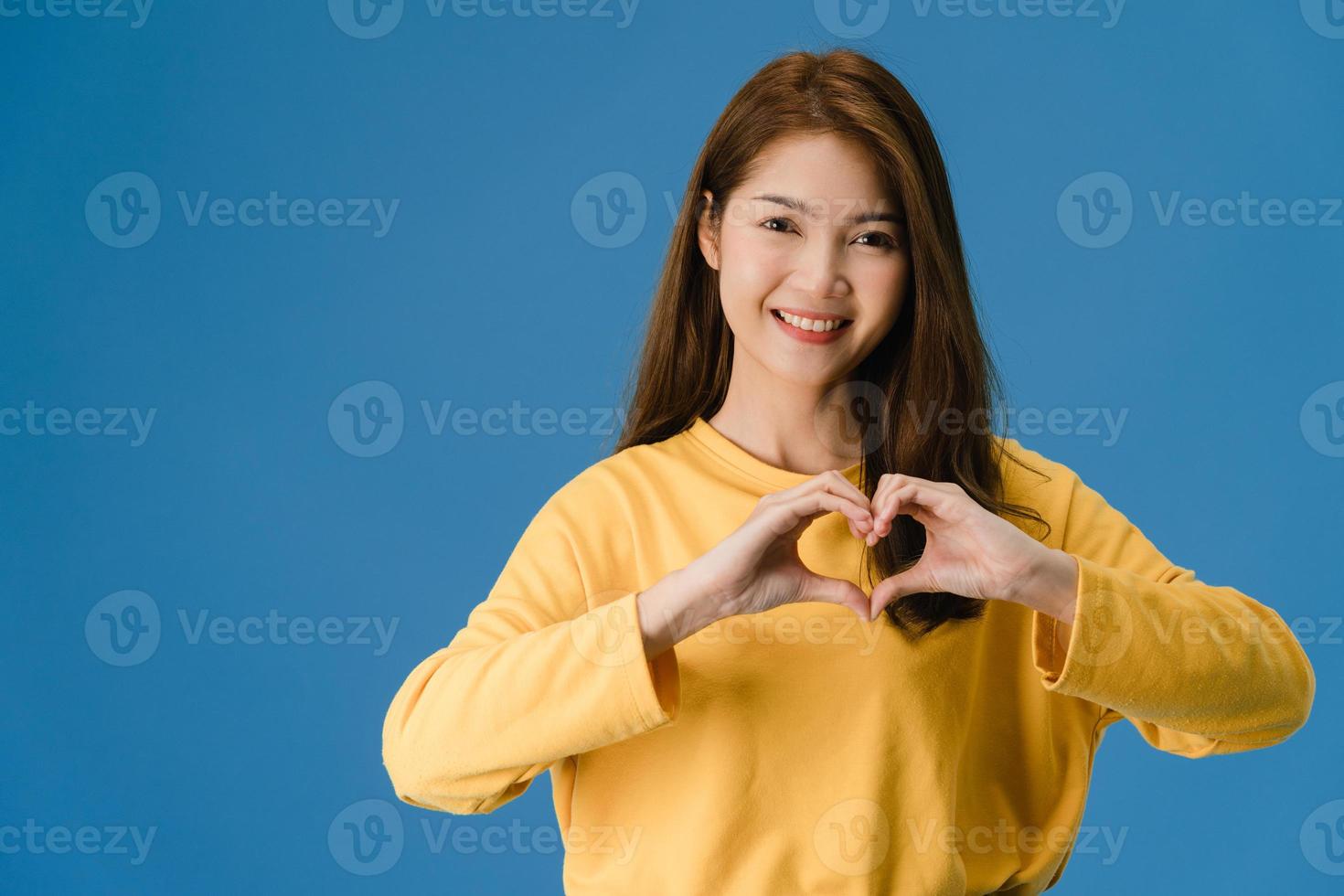 joven asiática muestra gesto de las manos en forma de corazón sobre fondo azul. foto