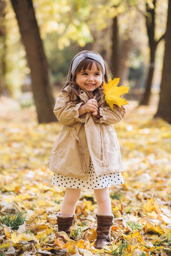 niña feliz sosteniendo una hoja de arce amarilla en el parque de otoño foto