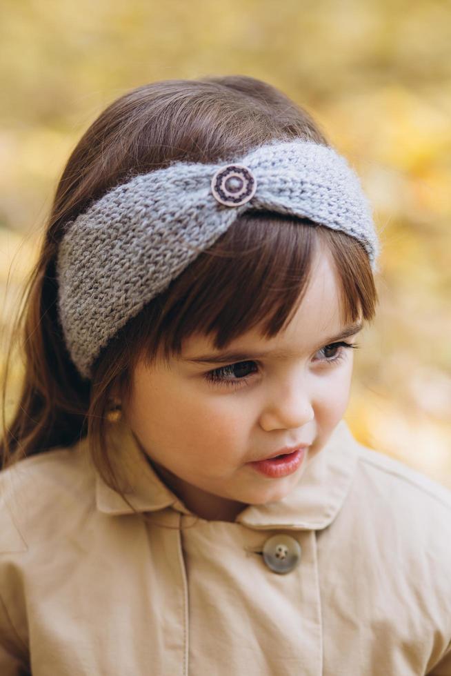 Niña feliz con un abrigo beige camina en el parque de otoño foto