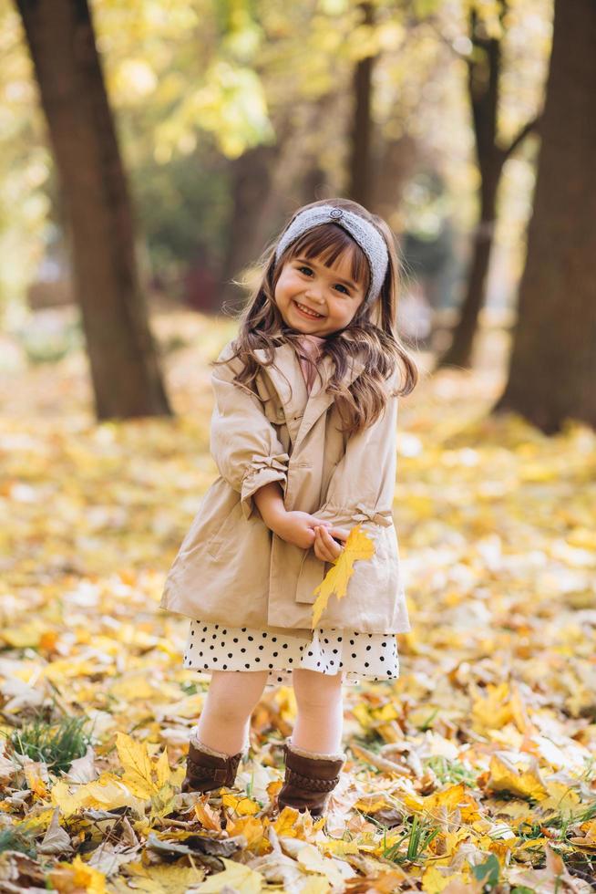 niña feliz sosteniendo una hoja de arce amarilla en el parque de otoño foto