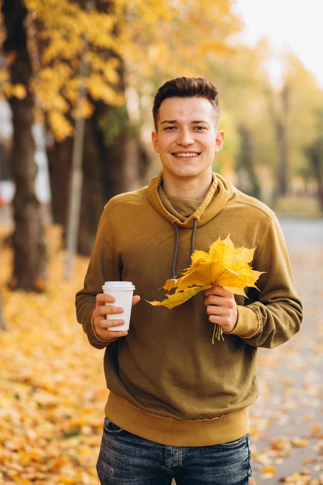 Guy with a bouquet of leaves smiling and drinking coffee in autumn photo