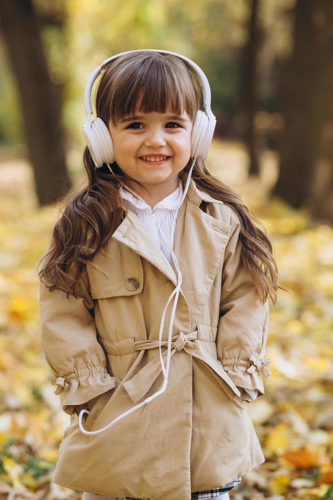Happy little girl listening to music on headphones in the autumn park photo
