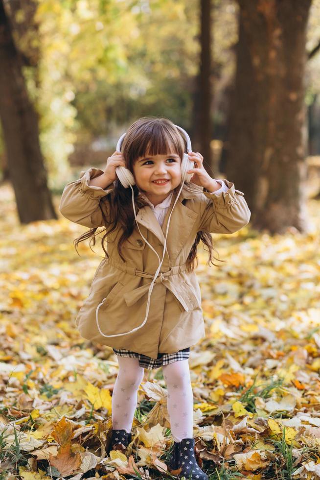 Happy little girl listening to music on headphones in the autumn park photo