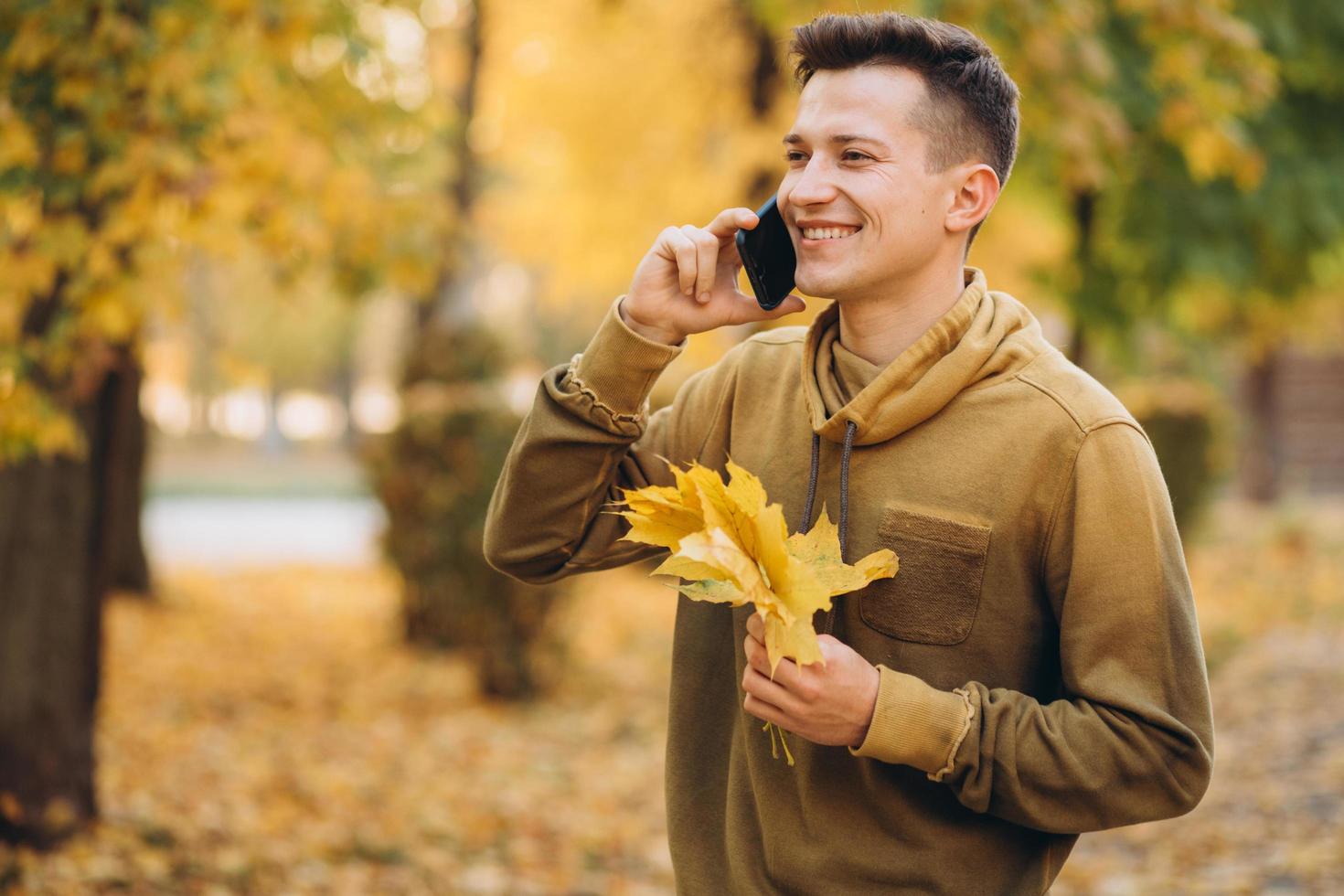 chico feliz sonriendo y hablando por teléfono en el parque de otoño foto